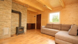 A log cabin interior with a stone fireplace, wooden flooring, a sofa, and a window with a view of trees. - Agroturystyka Katarzyna Tarasiewicz (Suwalki)