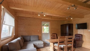 A cozy cabin interior with a wooden ceiling, a sofa, a dining table with chairs, a TV mounted on the wall, and a window. - Agroturystyka Katarzyna Tarasiewicz (Suwalki)