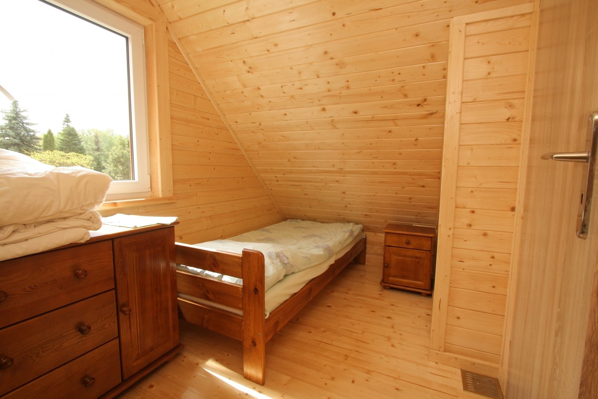 Una habitación pequeña con paneles de madera, una cama individual, un aparador y una ventana.