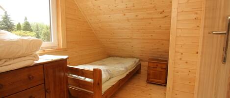 A small, wooden-paneled room with a single bed, a dresser, and a window.
