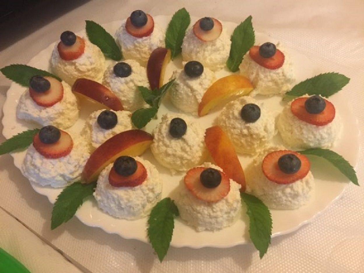 Een bord met dessertbolletjes, fruit toppings en muntblaadjes.