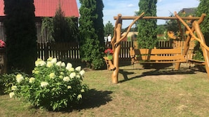 A wooden swing set in a backyard with a red-roofed house in the background. - Agroturystyka Katarzyna Tarasiewicz (Suwalki)