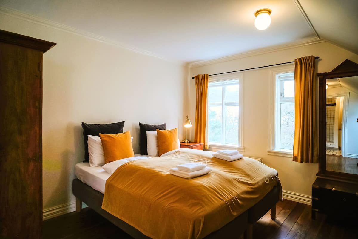 A bedroom with a bed, a nightstand, a window with curtains, and a mirror.