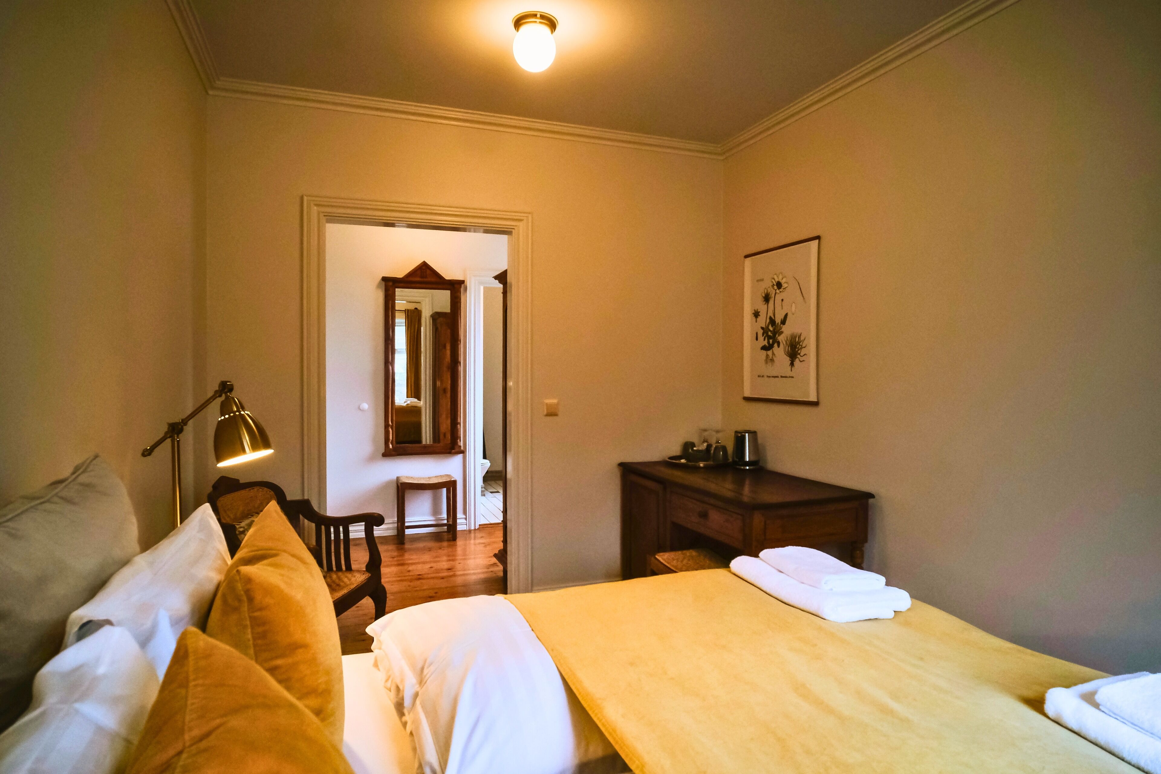 Une chambre d’hôtel avec un lit, une table de chevet, une lampe, une chaise, un bureau et un tableau encadré au mur.