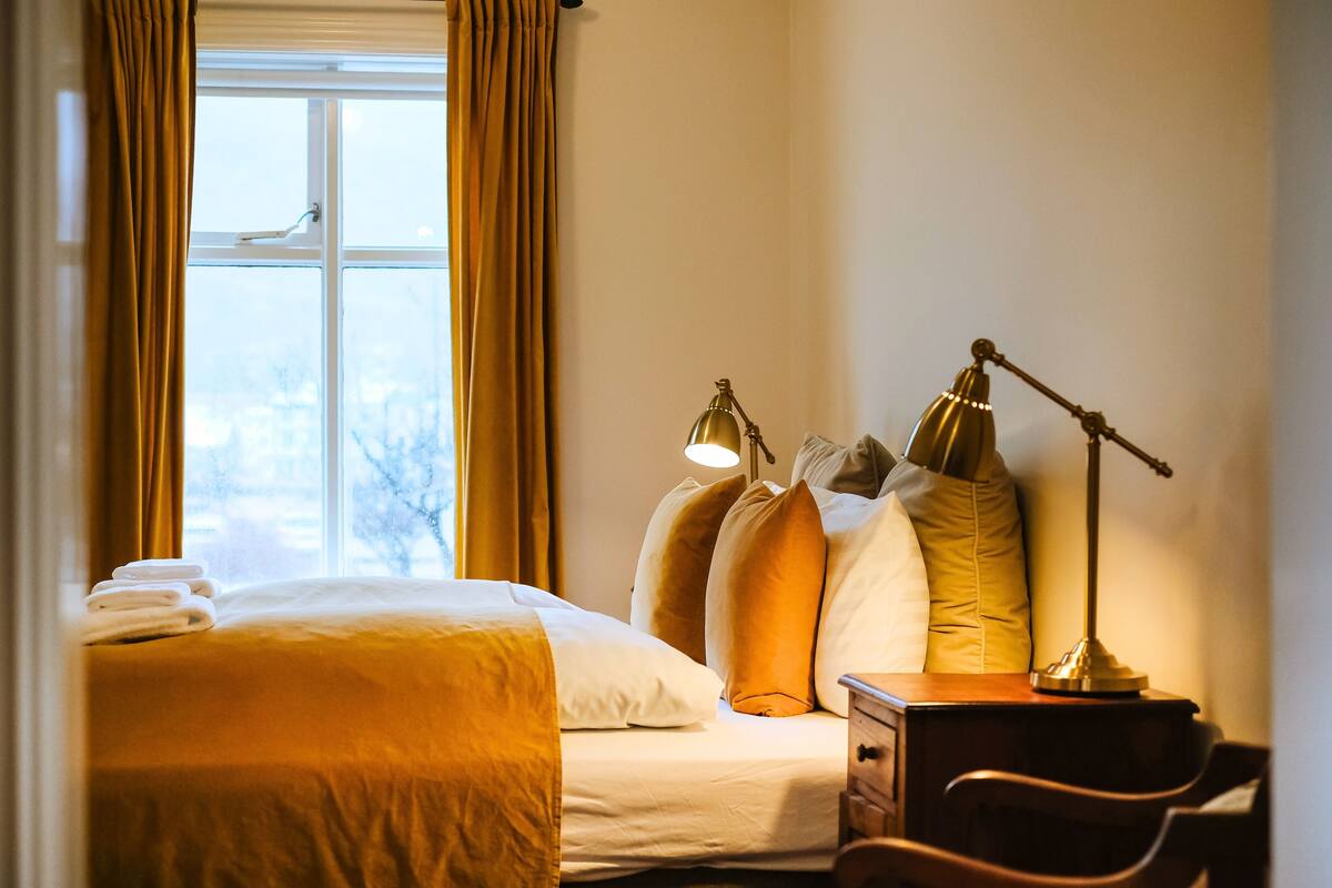 A hotel room with a bed, two bedside lamps, a nightstand, and a window with curtains.