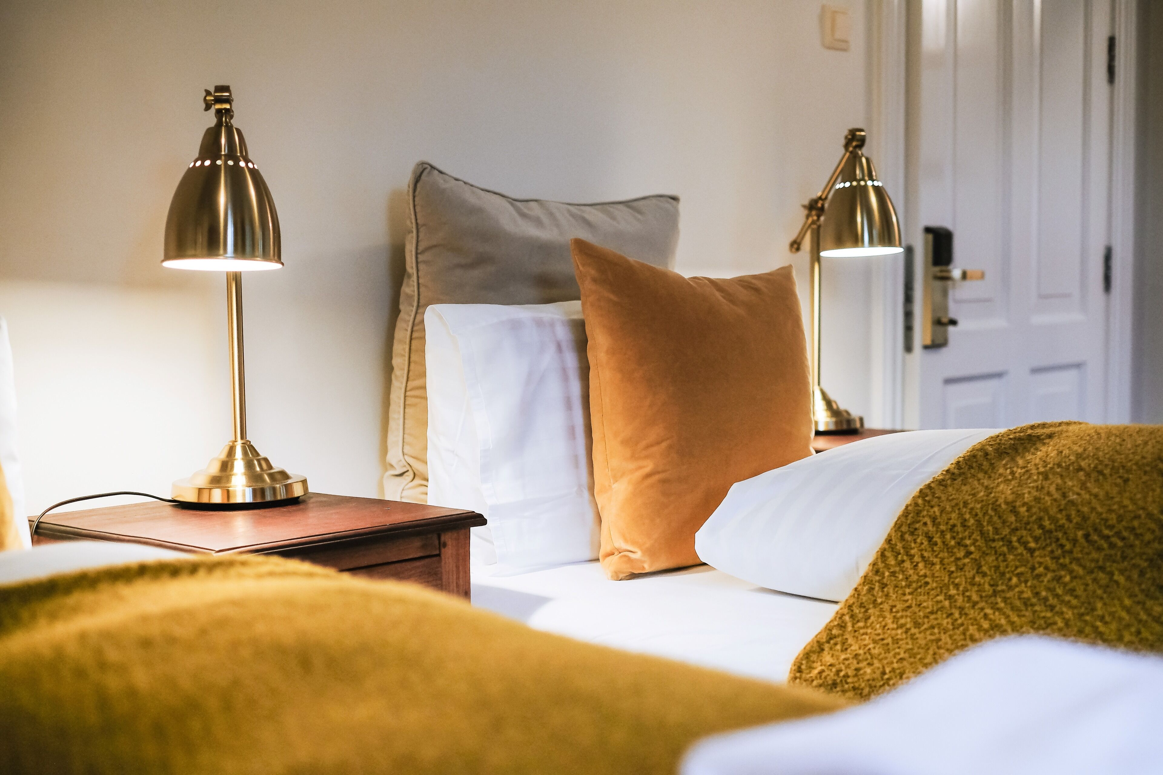 A neatly made bed with white and brown bedding, two bedside lamps, and a wooden nightstand.