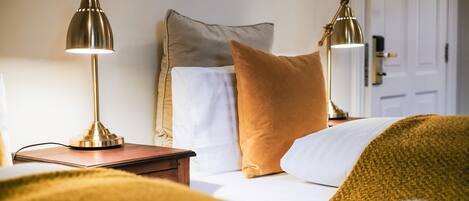 A neatly made bed with white and brown bedding, two bedside lamps, and a wooden nightstand.