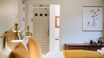 Une chambre d’hôtel comprenant un lit, une table de chevet, une salle de bain avec douche et une illustration botanique encadrée accrochée au mur.