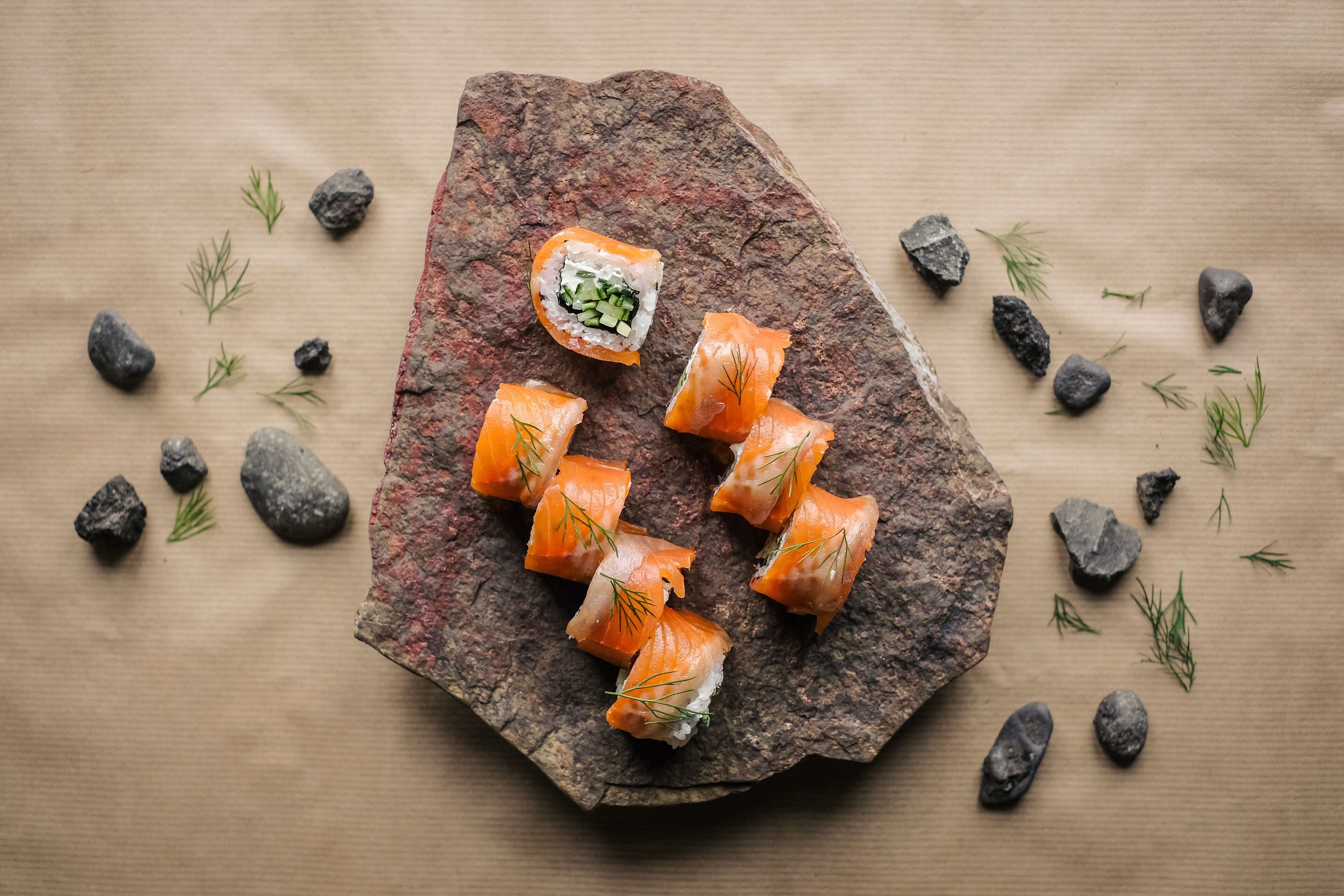 Sushi pieces on a rock with scattered rocks and green leaves around.