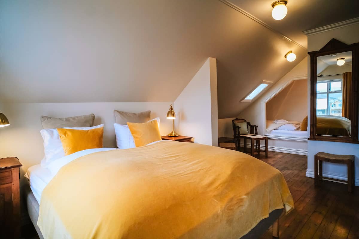A bedroom with a large bed, a nightstand, a lamp, a chair, and a mirror.