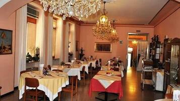 Une salle à manger avec des tables dressées pour le service, un lustre et des œuvres d’art encadrées accrochées aux murs.