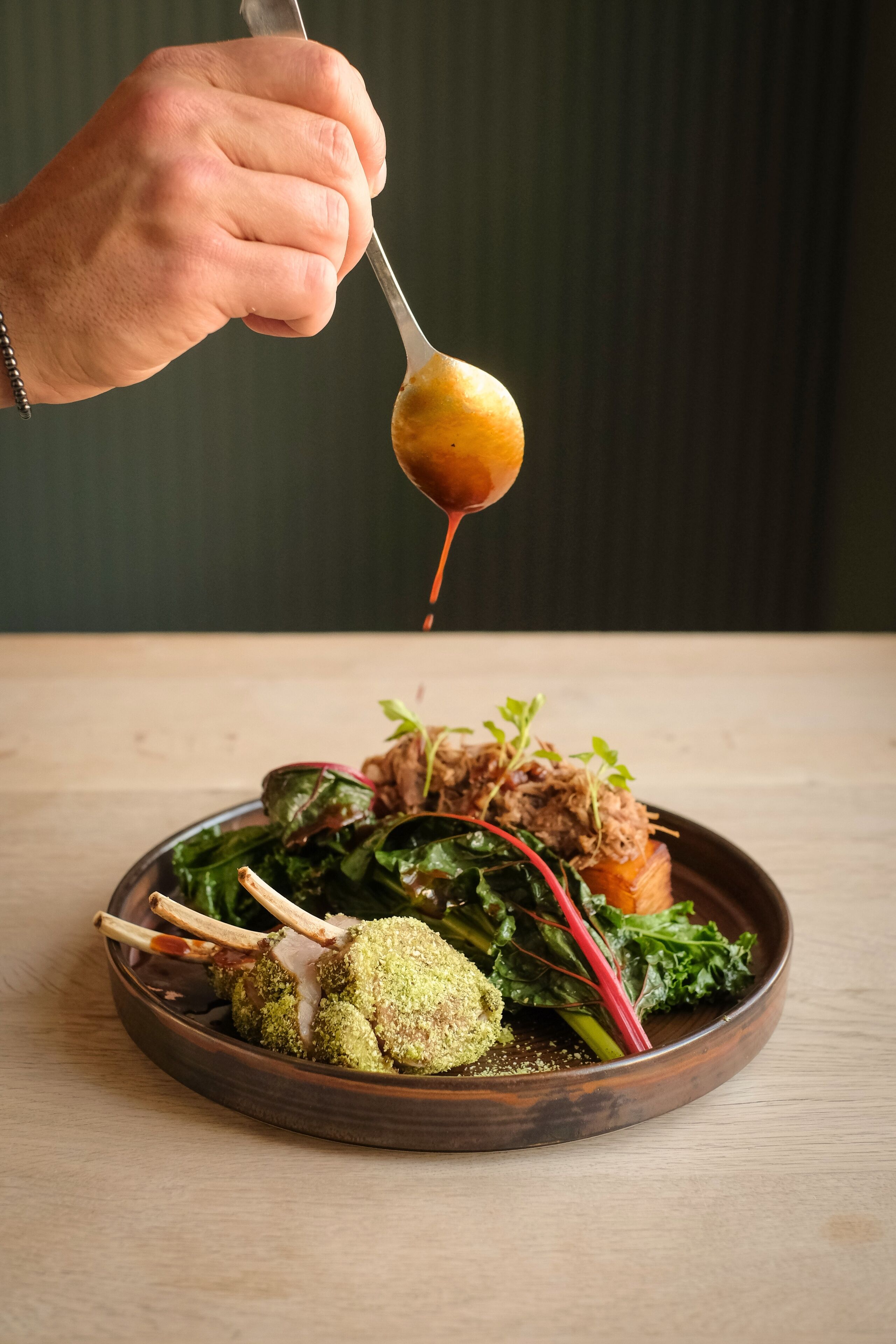 A person serving a dish with greens, meat, and a sauce.