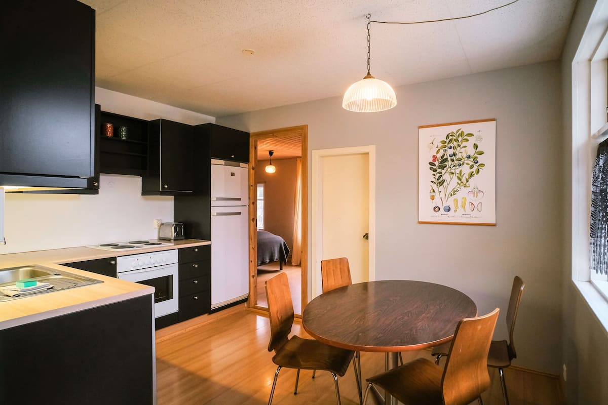 A compact kitchen with modern appliances, a dining area with a round table and chairs, and a hanging light fixture.