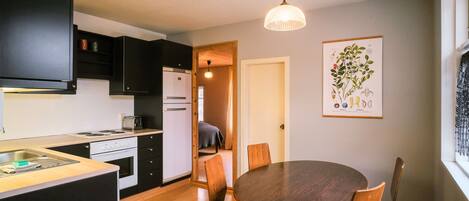 A compact kitchen with modern appliances, a dining area with a round table and chairs, and a hanging light fixture.