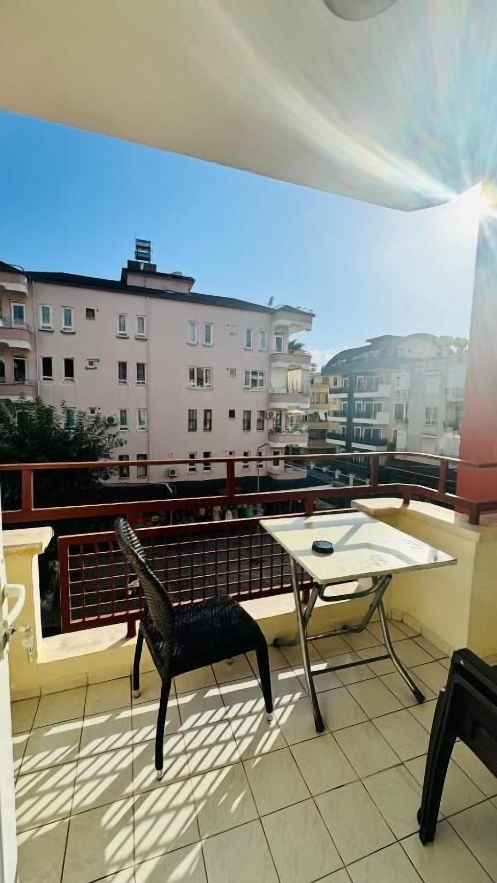 A balcony with a table and chairs, a view of buildings, and a clear sky.
