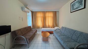 A living room with two sofas, a coffee table, a TV, and a bed with curtains.