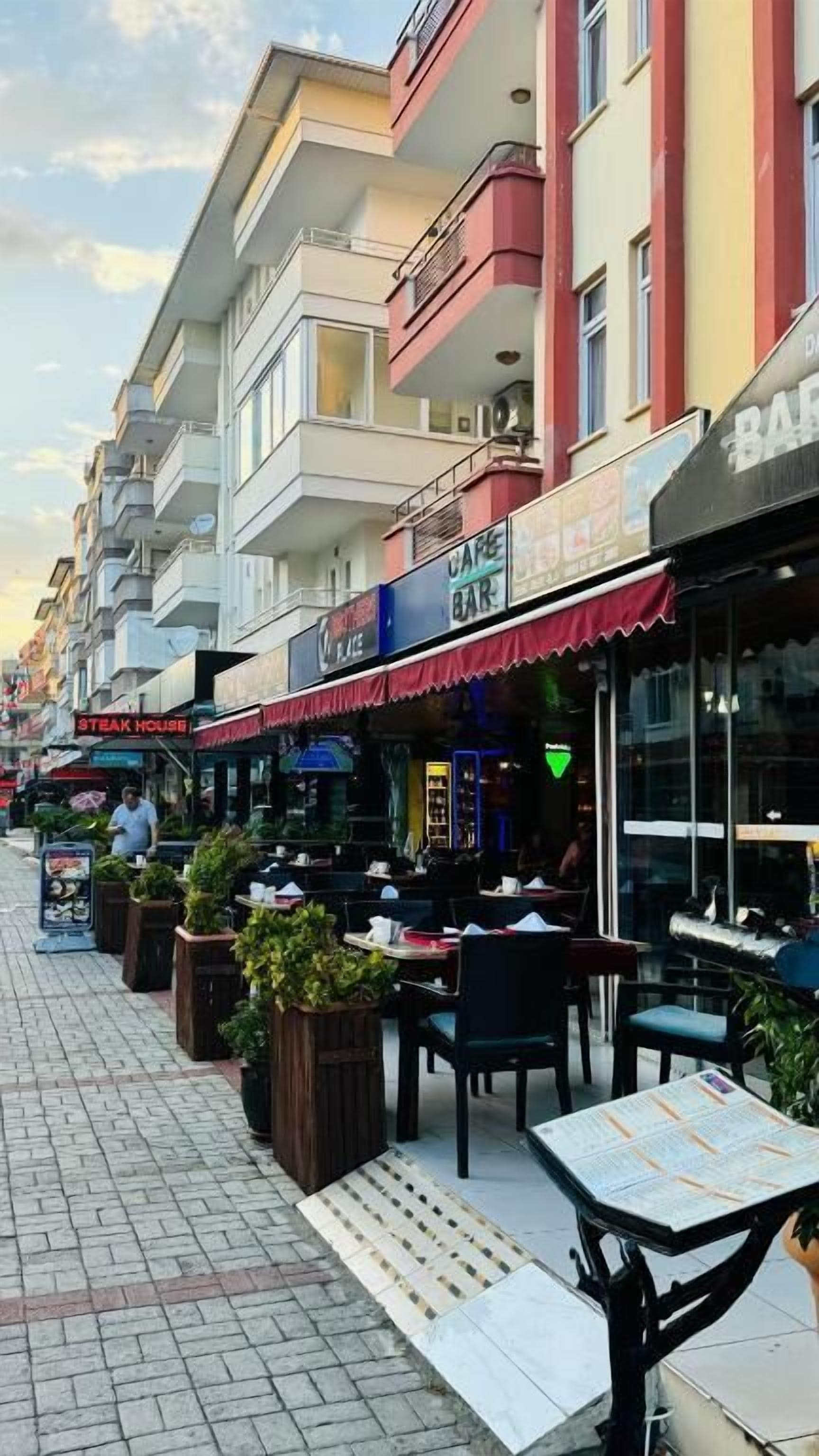 A street with outdoor seating at various establishments, including a steakhouse and a bar.