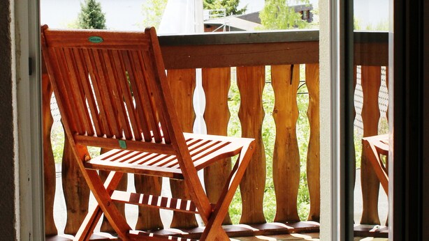A wooden chair on a balcony with a view of a lake and forest. - Hotel Jägerhof (Schluchsee)