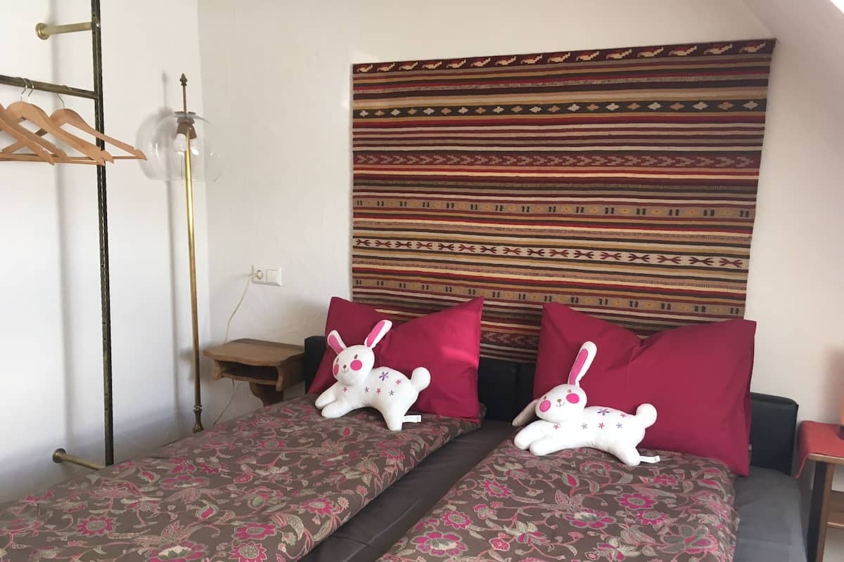 Een kamer met een bed, twee kussens, een hanglamp en een kamerbreed wandtapijt.
