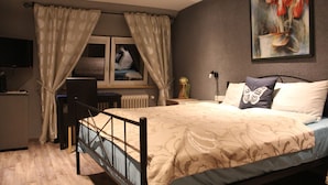 A bedroom with a bed, curtains, a painting, a desk, and a radiator. - Hotel Jägerhof (Schluchsee)