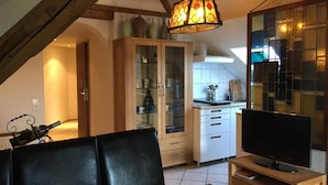 A dining area with a table and chairs, a television, and a kitchen in the background. - Hotel Jägerhof (Schluchsee)