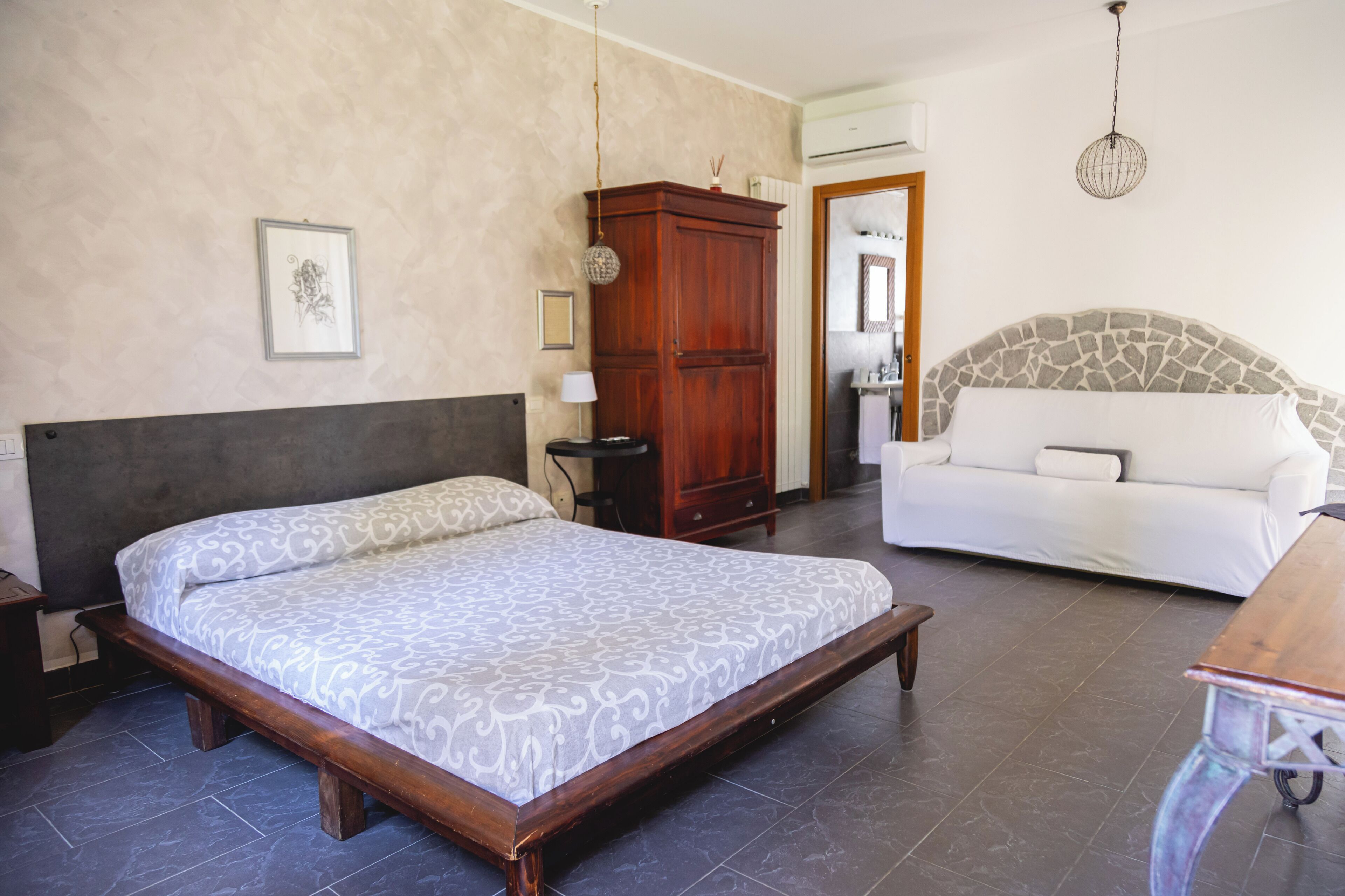 A bedroom with a bed, a wooden wardrobe, a white sofa, and a stone headboard.