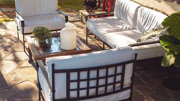A covered outdoor seating area with stone walls, a white sofa, a chair, and a table with a plant.