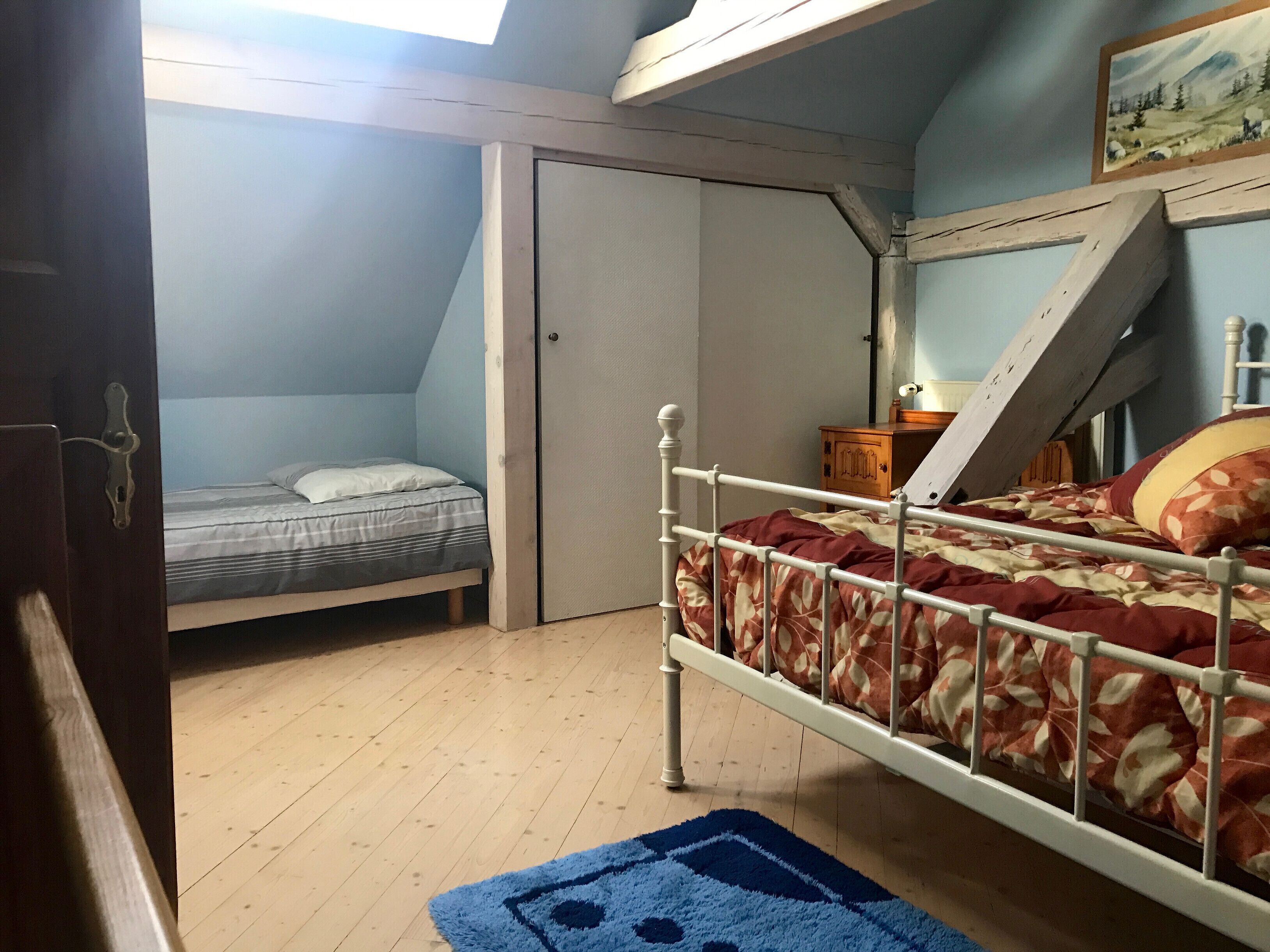 A bedroom with two beds, a wooden floor, a blue rug, and a painting on the wall.