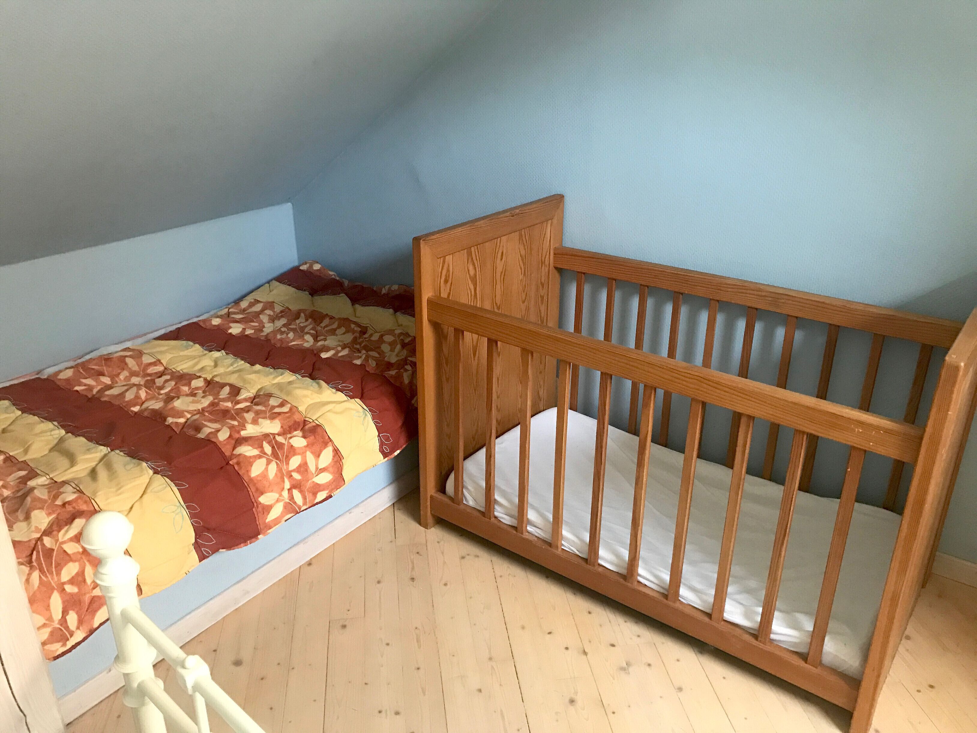 A small, single-room with a wooden crib and a bed with a patterned quilt.