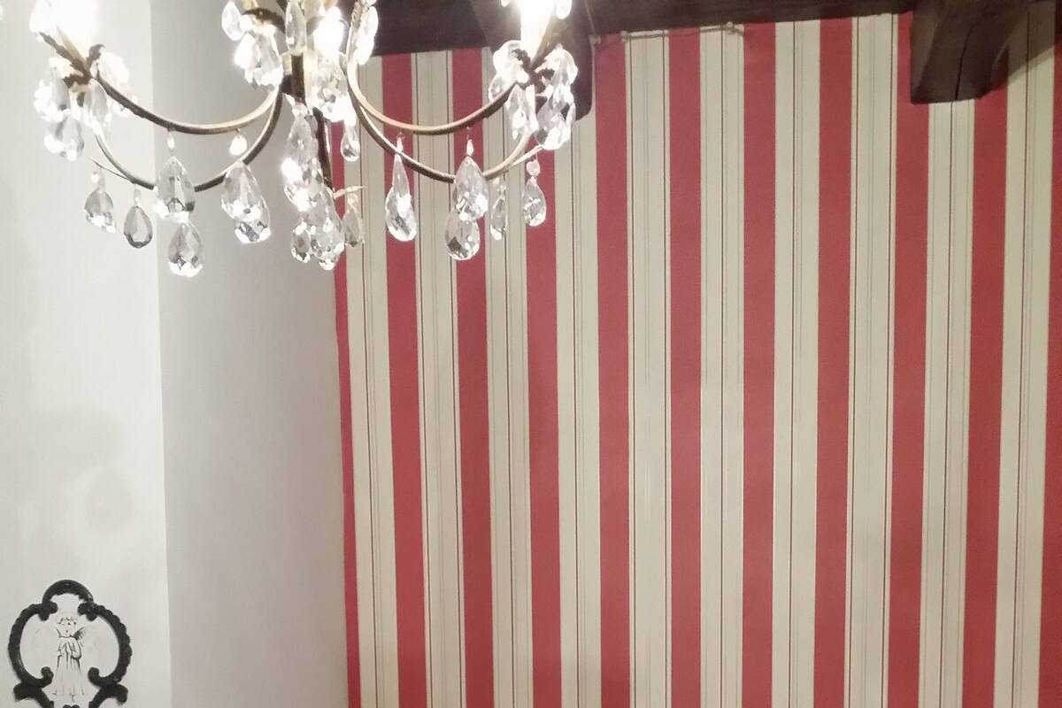Un dormitorio con papel tapiz a rayas, estructura de cama metálica, candelabro y aplique de pared.