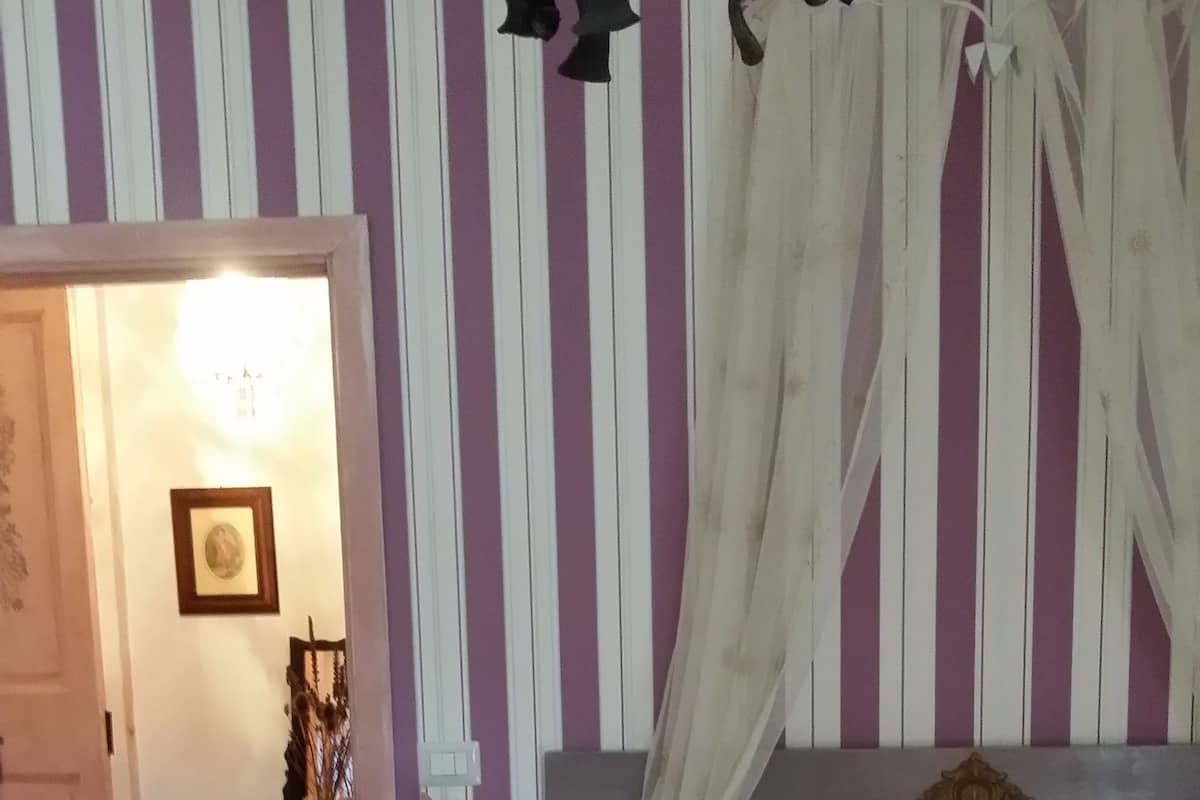 Un dormitorio con una cama, una mesita de noche, una lámpara, un marco de fotos y una cortina.