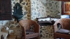 Un coin accueillant avec des fauteuils en osier, un mur en pierre, une étagère en bois ornée d’objets décoratifs et une horloge fixée au mur.