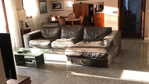 A living room with a sofa, a dining table with chairs, and a cabinet. There are framed pictures on the wall and a door with a frosted glass panel. - B&B Amy & Julie (Badia Polesine)