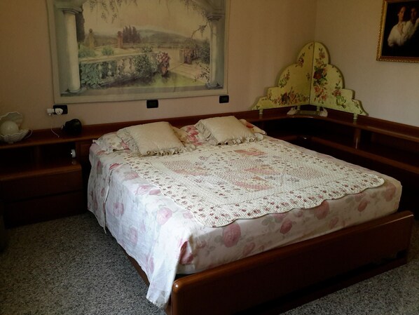 A bedroom with a wooden bed, floral bedding, a decorative headboard, a nightstand, and a painting on the wall. - B&B Amy & Julie (Badia Polesine)