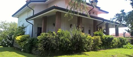 Una casa de dos pisos con un porche cubierto, columnas de ladrillo y un jardín bien cuidado.