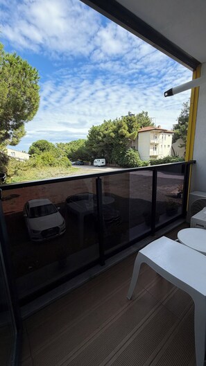 A balcony with a view of parked cars and buildings, a white table, and a fan. - Deluxe Beach Residence (Atakum)