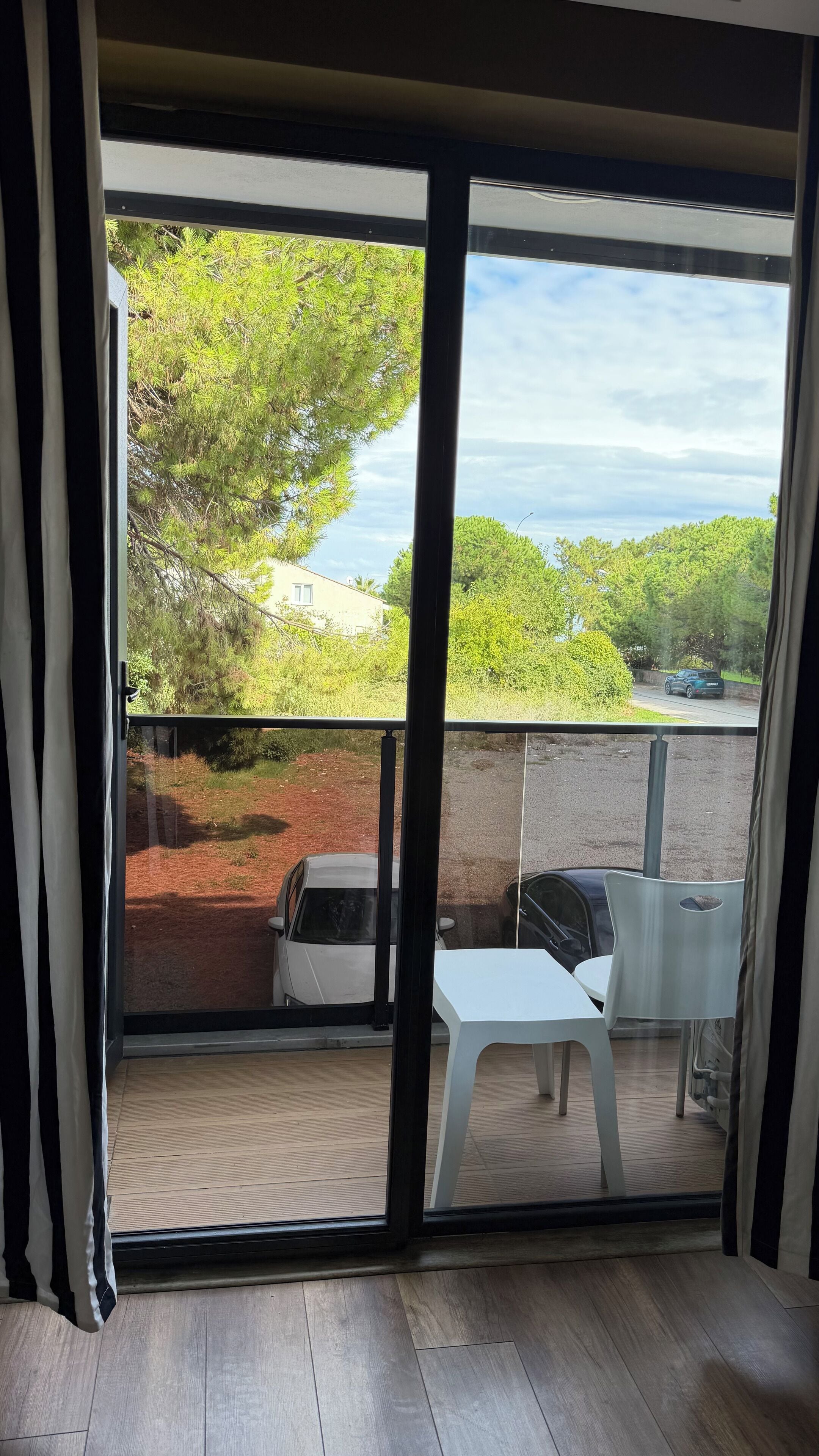 A balcony with a view of a parking area, a white table, and a white chair.