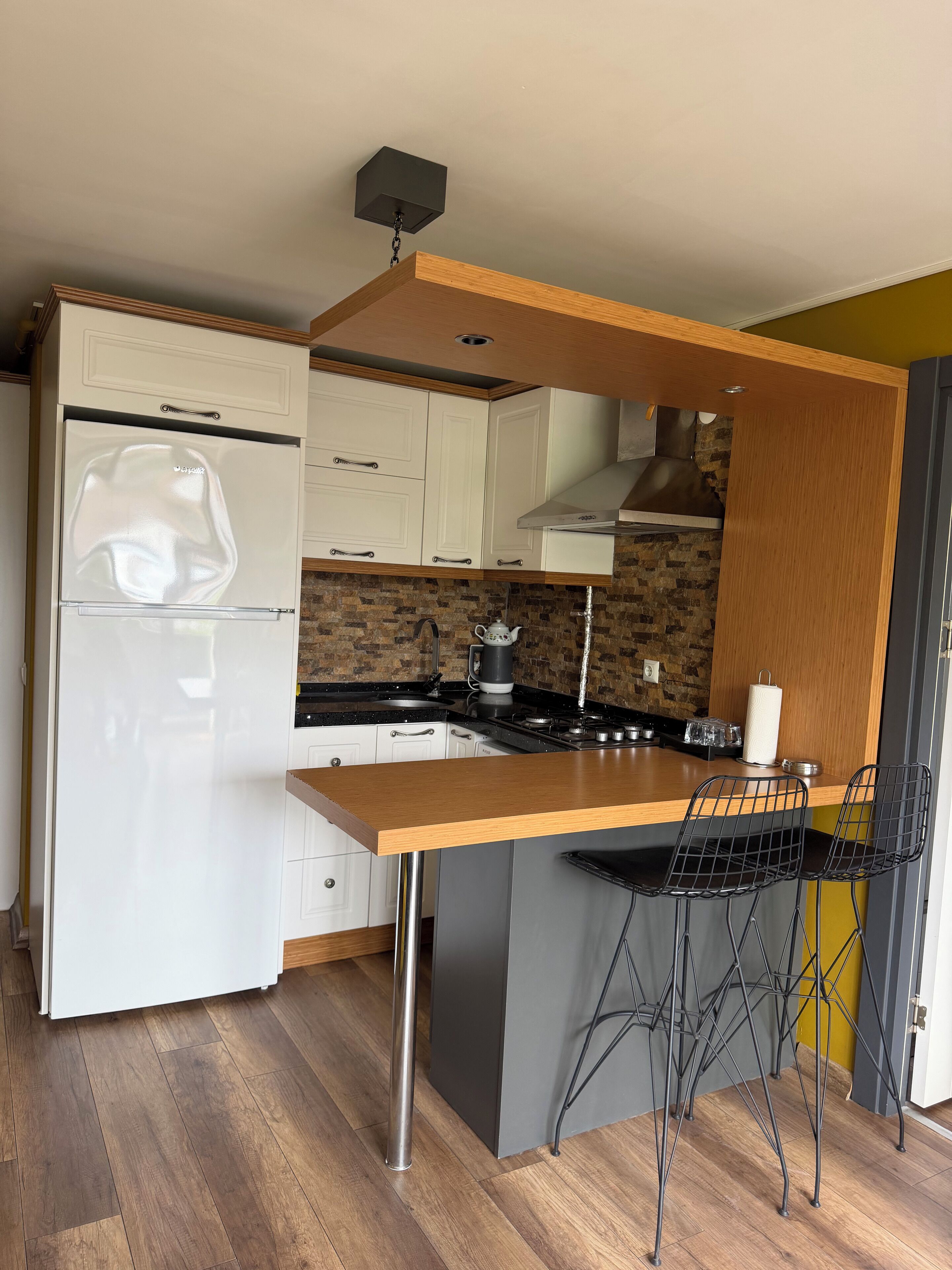 A compact kitchen with white cabinets, a stainless steel refrigerator, a wooden island with bar stools, and a brick backsplash.