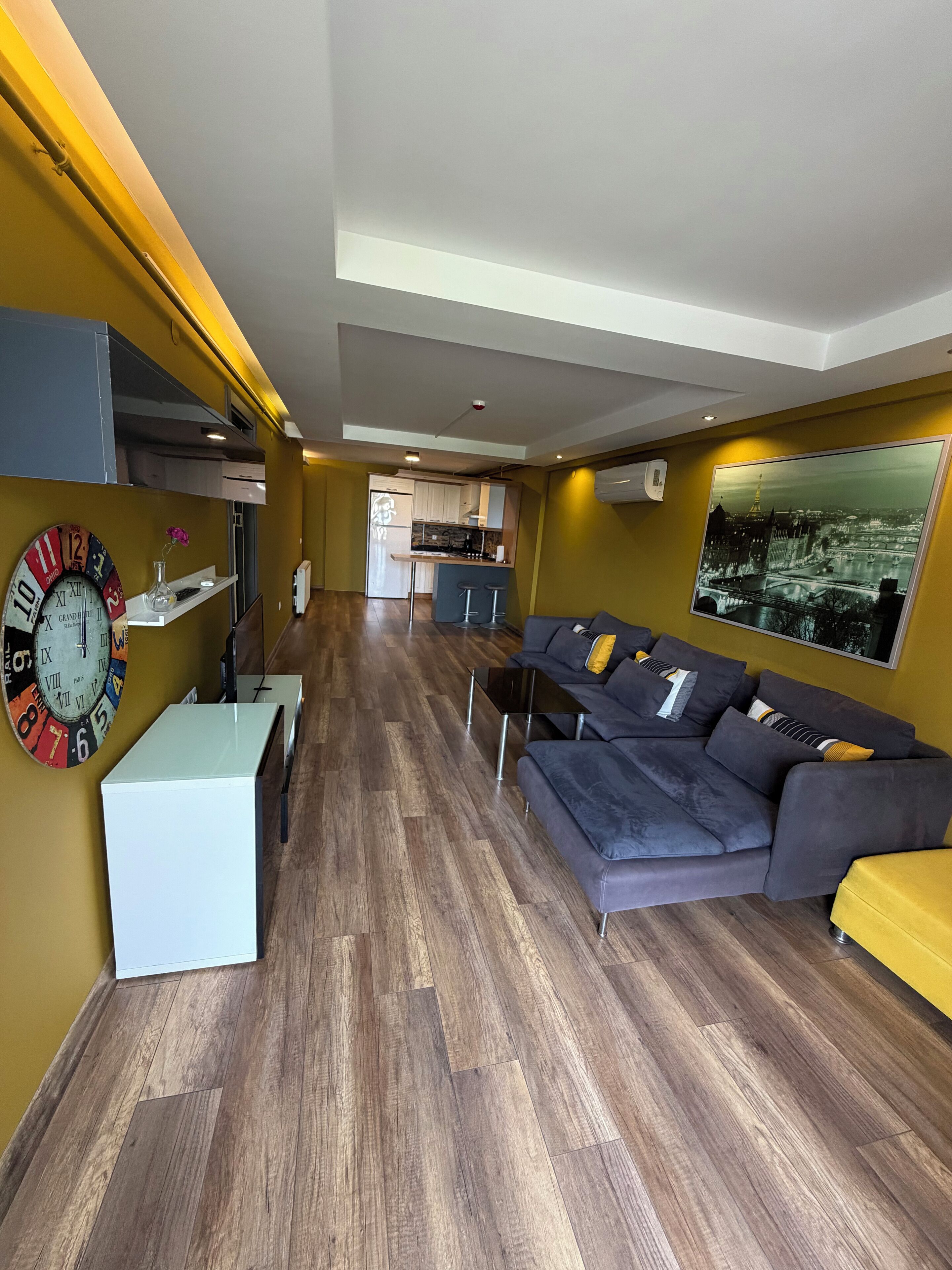 A modern living room with a grey sofa, a white coffee table, and a large wall clock.
