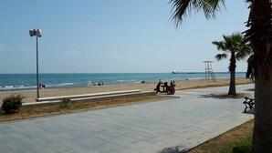 A paved walkway along a beach with palm trees, a distant pier, and a red scooter. - Deluxe Beach Residence (Atakum)
