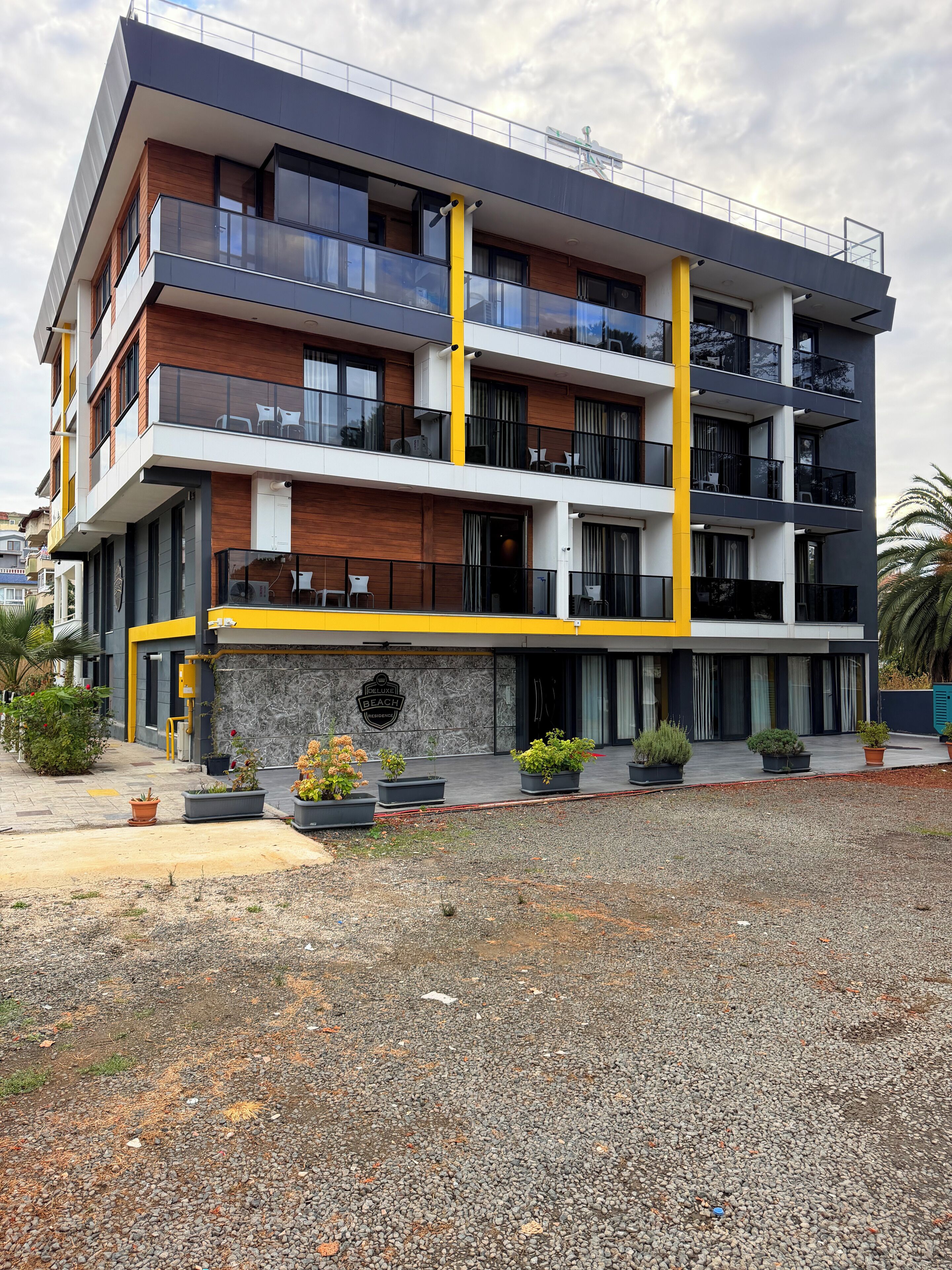 Un immeuble à plusieurs étages doté de balcons, d’une façade en pierre et d’un espace extérieur recouvert de gravier.