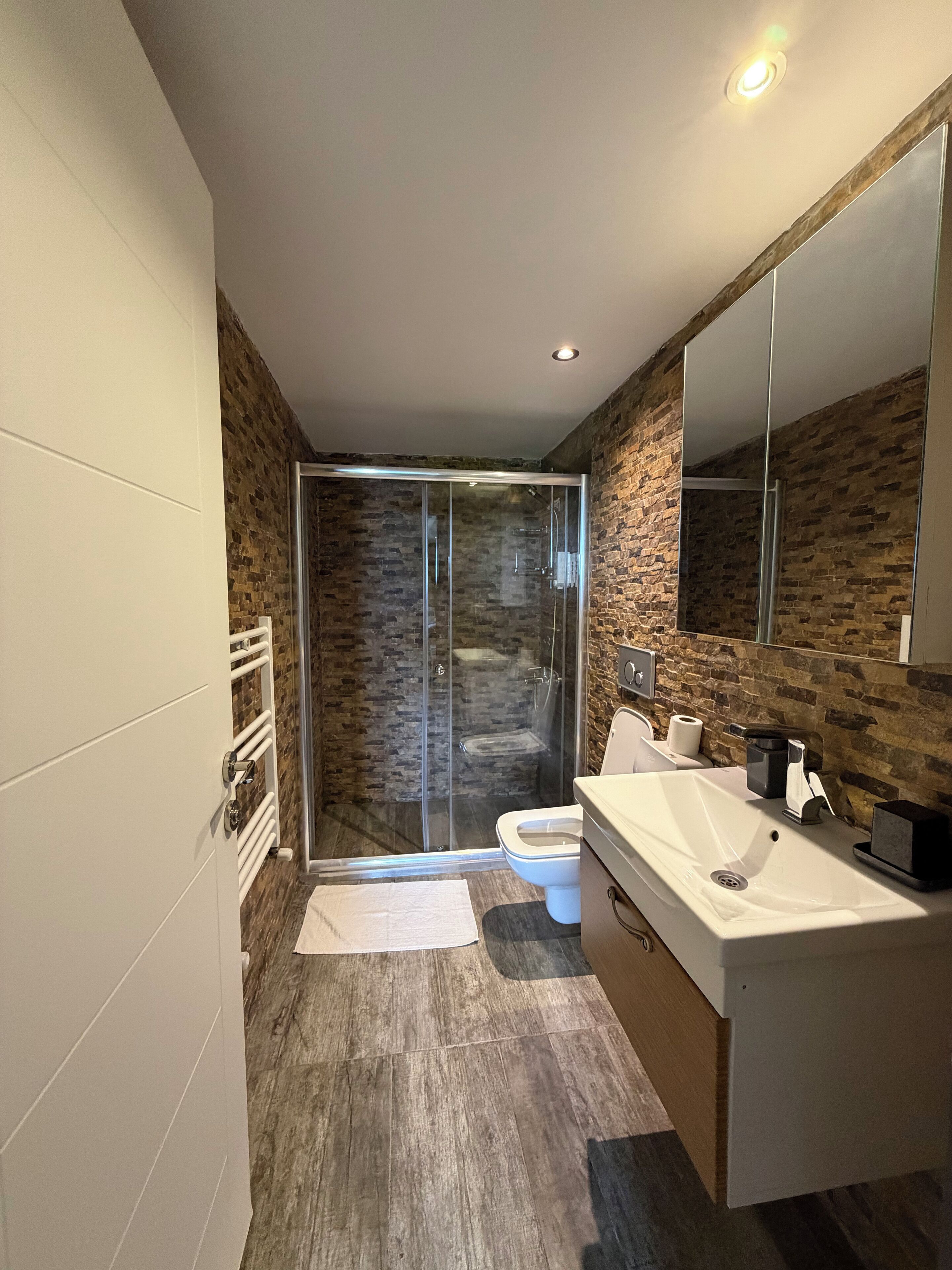 Un baño moderno con ducha envuelta en vidrio, un lavabo blanco y un espejo grande.
