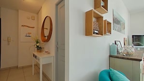 Un salon moderne avec un canapé blanc, un coussin turquoise et des étagères en bois où sont disposés divers objets.