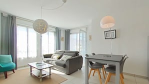 Un salon moderne comprenant un canapé, une table à manger et des chaises, de grandes fenêtres avec des rideaux et un luminaire suspendu.