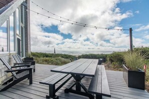 A wooden deck with a picnic table and chairs, overlooking a beach with a cloudy sky. - Lighthouse - Oceanfront, stunning, updated classic (Cloverdale)