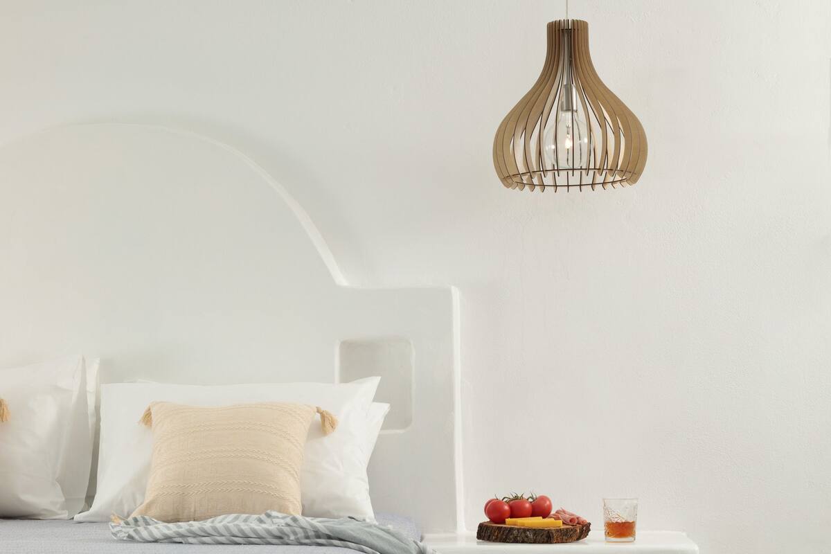 A modern bedroom with a bed, white nightstands, a fruit bowl, and a hanging light fixture.