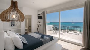 A bedroom with a large balcony, a bed, a TV, and a view of the sea. - Manios Suites (Naxos)