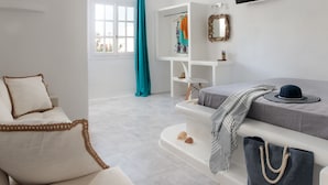 A modern, minimalist bedroom with a bed, a seating area, a TV, and a wardrobe. - Manios Suites (Naxos)