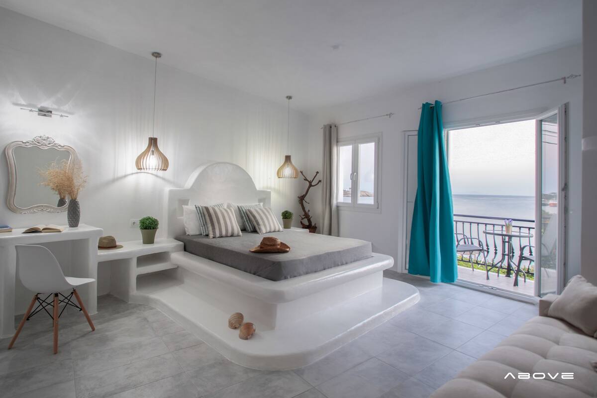 A modern bedroom with a large bed, a desk, and a view of the sea.