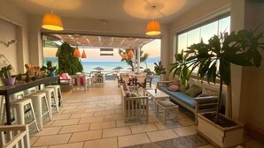 A spacious indoor area with a view of the sea, featuring a bar, seating arrangements, and potted plants. - Manios Suites (Naxos)